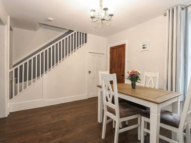 A dining area with a wooden table and white chairs under a staircase at Hunny Cottage in Hunstanton