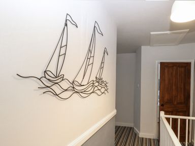A hallway with striped carpet a wooden door and metal wall art of boats on waves at Hunny Cottage in Hunstanton
