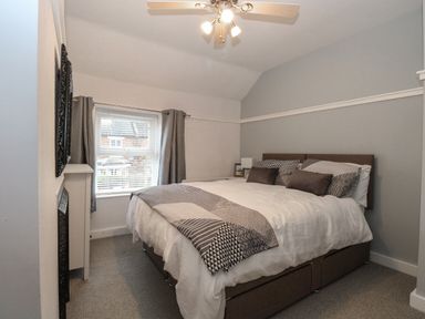 A bedroom with a double bed next to a window with curtains and a ceiling fan at Hunny Cottage Hunstanton