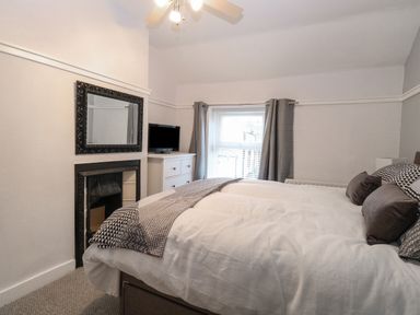 A bedroom with a bed pillows and a blanket a window with curtains a chest of drawers a television and a wall mirror at Hunny Cottage in Hunstanton