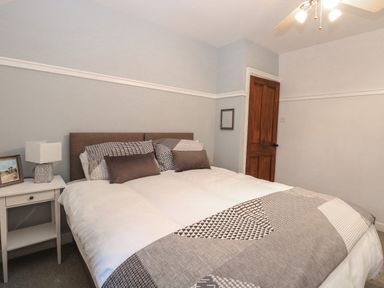 A bedroom with a large bed pillows beside a nightstand with a lamp and framed picture at Hunny Cottage in Hunstanton