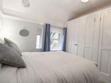 A bedroom with a bed against a polka dot wall a window with blue curtains and white wardrobes at Hunny Cottage in Hunstanton