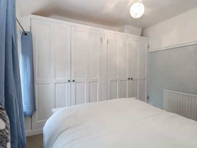 A bedroom with a bed in front of white wardrobes blue curtains and a radiator at Hunny Cottage in Hunstanton