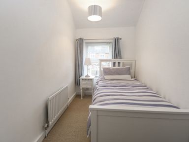 A small bedroom with a single bed striped bedding a bedside table with lamp and a window with curtains at Hunny Cottage in Hunstanton