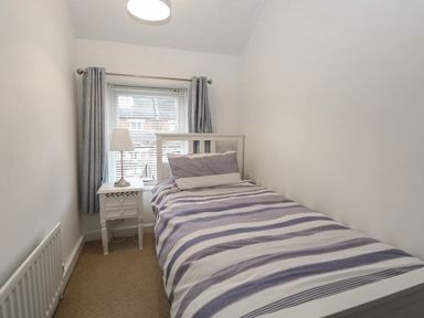 A small bedroom with a single bed striped bedding bedside table with lamp and window with curtains at Hunny Cottage in Hunstanton