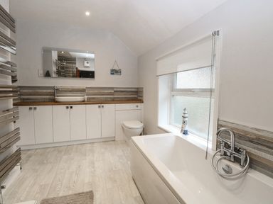 A bathroom with a bathtub a toilet a sink with cabinets and a window at Hunny Cottage in Hunstanton