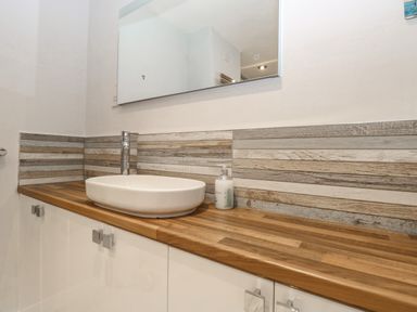 A bathroom countertop with a white oval sink wooden surface and striped backsplash at Hunny Cottage in Hunstanton
