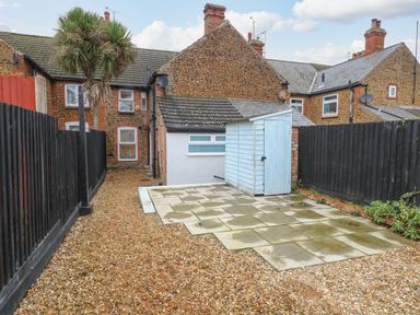 A gravel backyard with a small blue shed and black wooden fences at Hunny Cottage in Hunstanton