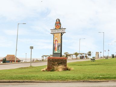 A sign reading Hunstanton on a brick base on grass near a road with benches and buildings in the background in Hunstanton