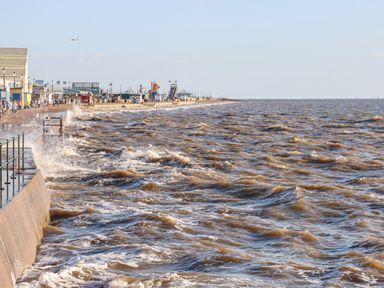 A rough sea with waves crashing against a sea wall and a promenade with buildings and people at Hunny Cottage in Hunstanton
