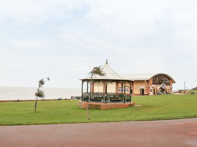 A green lawn with a pavilion near a beach and a large building in the background at Hunny Cottage in Hunstanton