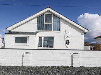 The front exterior of a white house with multiple windows and a surfboard mounted on the wall at Sea Scape in Dinas Dinlle
