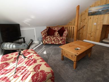 A loft living area with a television on a stand a wooden coffee table a patterned armchair and a telescope on a matching patterned ottoman at Sea Scape in Dinas Dinlle