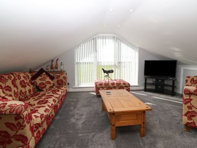 A living room with patterned sofas a wooden coffee table a television on a stand and a telescope near a window at Sea Scape in Dinas Dinlle