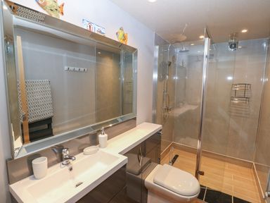 A bathroom with a sink countertop cabinet toilet and glass shower enclosure at Sea Scape in Dinas Dinlle