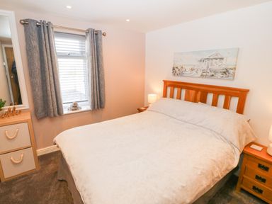 A bedroom with a bed a wooden headboard curtains on the window and nightstands at Sea Scape in Dinas Dinlle