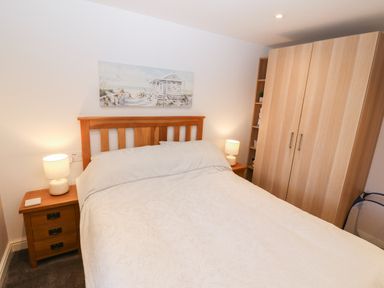 A bedroom with a bed, two bedside tables with lamps, a wooden wardrobe and a beach painting on the wall at Sea Scape in Dinas Dinlle