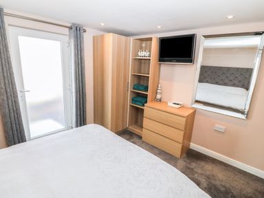 A bedroom with a bed wardrobe chest of drawers wall mounted tv and a large mirror at Sea Scape in Dinas Dinlle