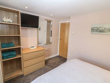 A bedroom with a wooden dresser shelves a wall-mounted television a mirror and a door at Sea Scape in Dinas Dinlle