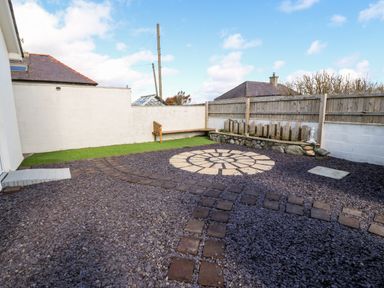 An outdoor patio area with stone tiles and gravel a wooden bench artificial grass and a wooden fence at Sea Scape in Dinas Dinlle
