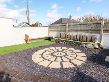 A backyard with circular stone patio a wooden bench artificial grass and a stone planter at Sea Scape in Dinas Dinlle