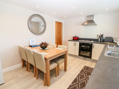 A kitchen with a wooden dining table and six chairs a round wall mirror and cooking appliances at Sea Scape in Dinas Dinlle