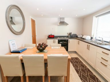 A kitchen with a dining table and beige chairs next to white cabinets and a window at Sea Scape in Dinas Dinlle