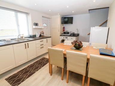A kitchen with white cabinets a dining table with six chairs and a wall mounted television at Sea Scape in Dinas Dinlle