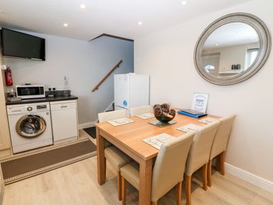 A dining area with a wooden table and six chairs next to a kitchen with a washing machine microwave dishwasher and a refrigerator at Sea Scape in Dinas Dinlle