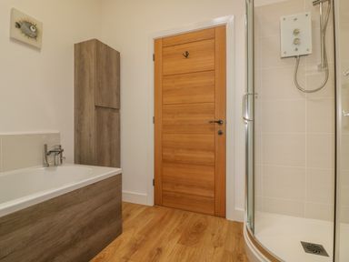 A bathroom with a wooden door bathtub wooden storage cabinet and a glass shower cubicle at Woodhall in Cardinham