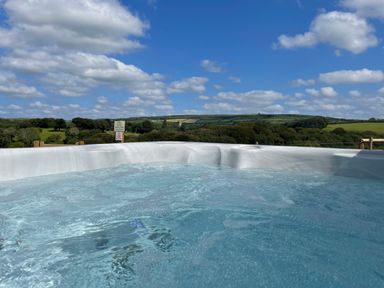 An outdoor hot tub with bubbling water overlooking a green landscape with trees and fields at Woodhall in Cardinham