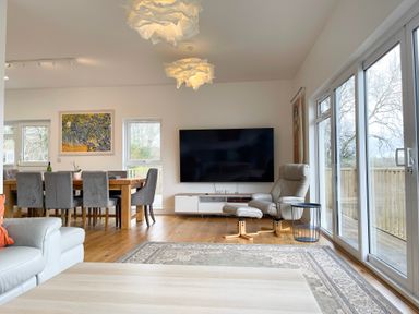 A living room with a dining table and chairs a large television and reclining chair at Woodhall in Cardinham