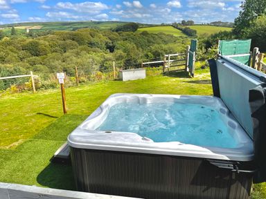 An outdoor hot tub on a grassy area with rolling hills and trees in the background at Woodhall in Cardinham