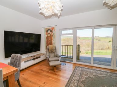 A living room with a large wall mounted television a recliner chair with a small table beside sliding glass doors and a wooden floor at Woodhall in Cardinham