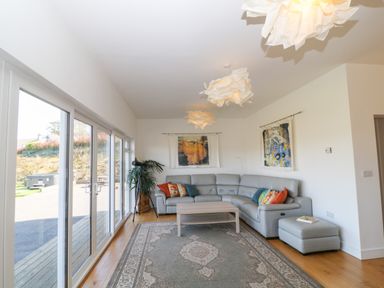 A living room with a gray sectional sofa colorful pillows a wooden coffee table and large glass doors at Woodhall in Cardinham