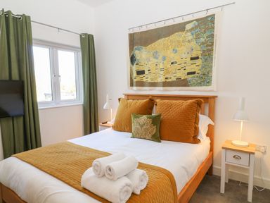 A bedroom with a double bed green curtains bedside tables with lamps and a wall hanging at Woodhall in Cardinham