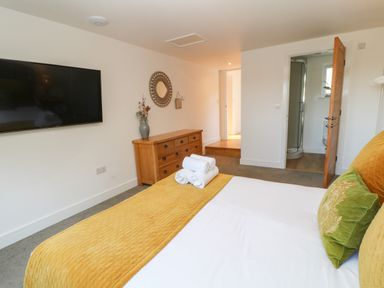 A bedroom with a bed and folded towels on the bed a wooden dresser and a wall-mounted television at Woodhall in Cardinham