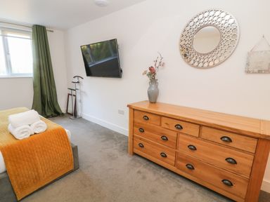 A bedroom with a wooden dresser with a vase of flowers and a decorative circular mirror above it at Woodhall in Cardinham