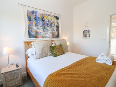 A bedroom with a bed with decorative pillows bedside tables lamps a colorful wall hanging and rolled towels at Woodhall in Cardinham