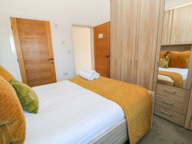 A bedroom with a bed covered by a mustard quilt and green pillows wooden wardrobe with mirror and wooden doors at Woodhall in Cardinham