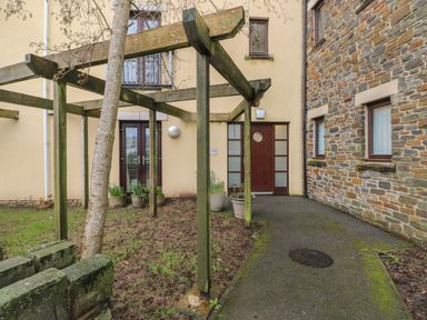 An outdoor area with wooden pergola plants in pots and a pathway leading to brown doors at 2 Chandlers Yard Burry Port