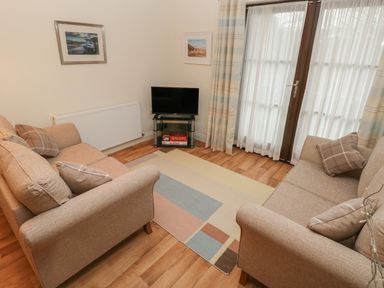 A living room with two beige sofas cushions a small television on glass stand and a patterned rug at 2 Chandlers Yard in Burry Port