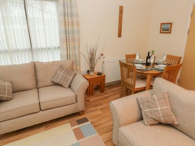 A living room with two beige sofas, a small wooden table with a vase, and a dining table set for four at 2 Chandlers Yard in Burry Port