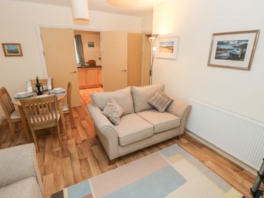 A living room with a sofa a dining table set and open doors leading to a kitchen at 2 Chandlers Yard in Burry Port