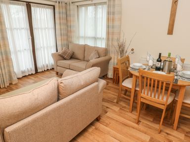 A living room with two beige sofas near windows and a wooden dining table set with plates and wine bottles at 2 Chandlers Yard in Burry Port