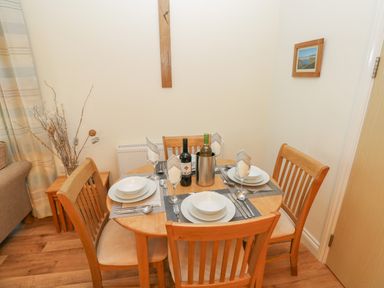 A dining area with a round wooden table set with plates glasses cutlery and two bottles of wine at 2 Chandlers Yard in Burry Port