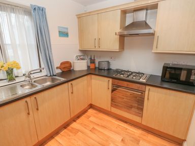 A kitchen with wooden cabinets black countertops a gas stove oven microwave sink and blue curtains at 2 Chandlers Yard in Burry Port
