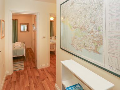 A hallway with wooden floor leading to two bedrooms and a large wall map with a white shelf below at 2 Chandlers Yard in Burry Port