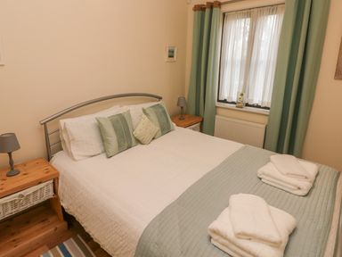 A bedroom with a double bed with pillows and folded towels by a window with curtains at 2 Chandlers Yard in Burry Port