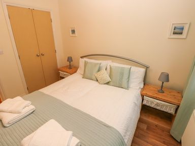 A bedroom with a double bed pillows bedside tables lamps and a closed wooden closet at 2 Chandlers Yard in Burry Port